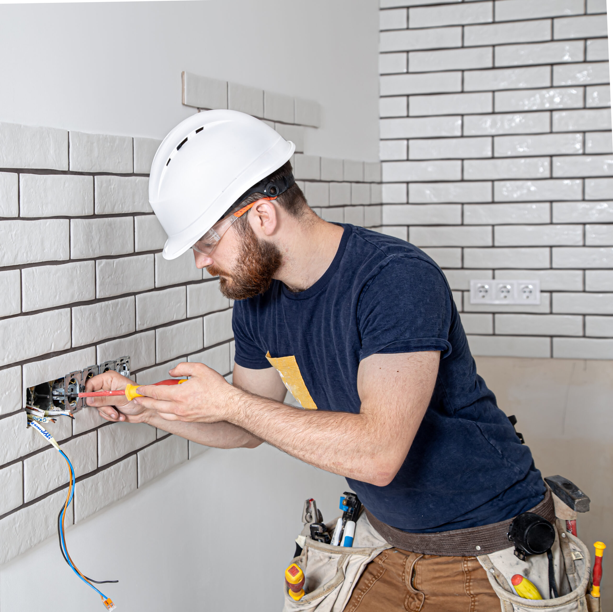 Electrician construction worker with a beard in overalls during the installation of sockets. Home renovation concept.